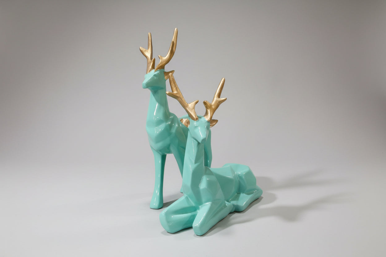 Two turquoise deer figurines with gold antlers on a white background