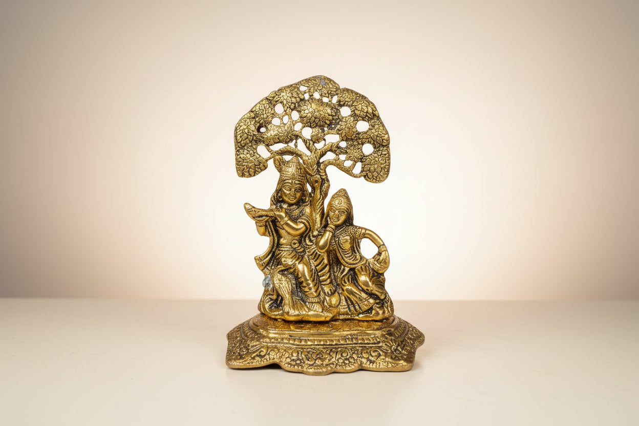 Gold-colored statue of a seated figure under a tree on a white background