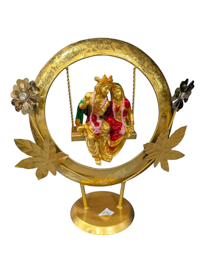 Agiftshop golden Radha Krishna jhula statue with intricate details, adorned with garlands, seated on a swing within a decorative circular frame.