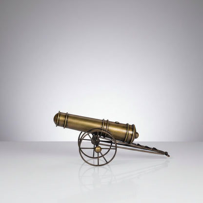 A bronze-colored metal showpiece designed to resemble an iron cannon with wheels and a barrel, mounted on a spherical base.