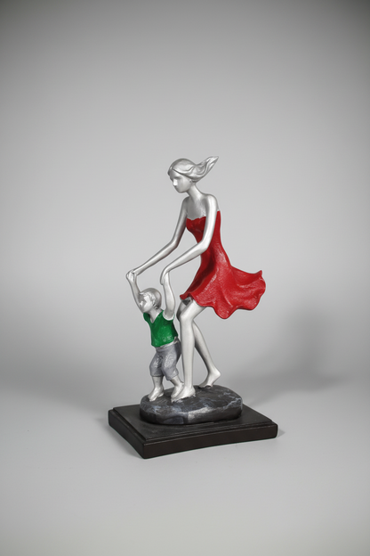 A resin figurine of a mother holding her child, both with neutral-colored clothing, displayed on a tabletop.