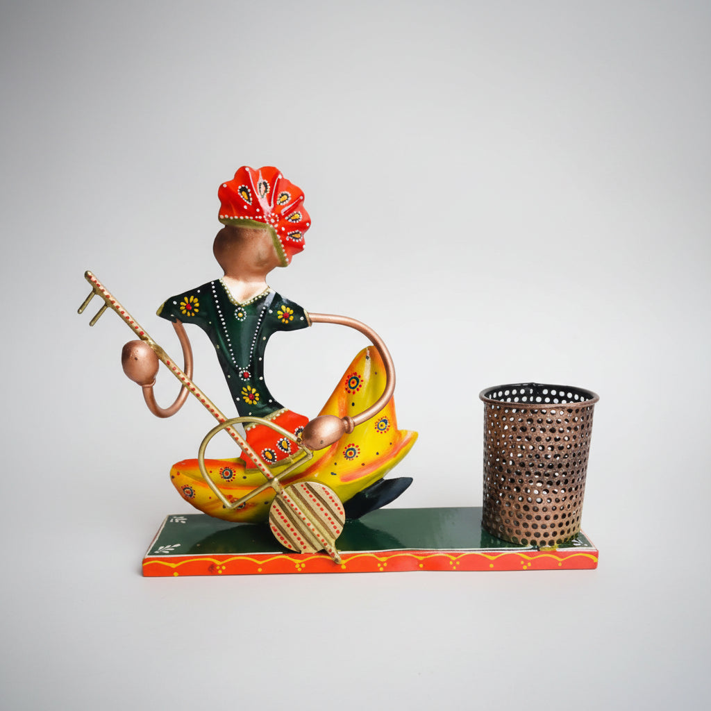 A decorative pen holder stand featuring a cultural figure playing a musical instrument, seated on a colorful, patterned surface holding a bin.