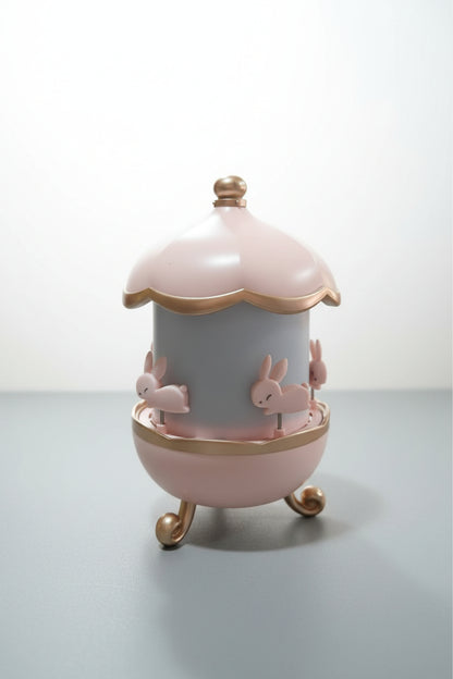 A Bunny Carousel Night Light Projector with a pink and white color scheme, featuring rabbit figures and a gold trim on the top.