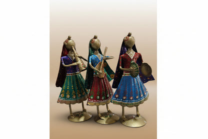 A set of three metal musician small dolls in various colored traditional attire, positioned on a tabletop.