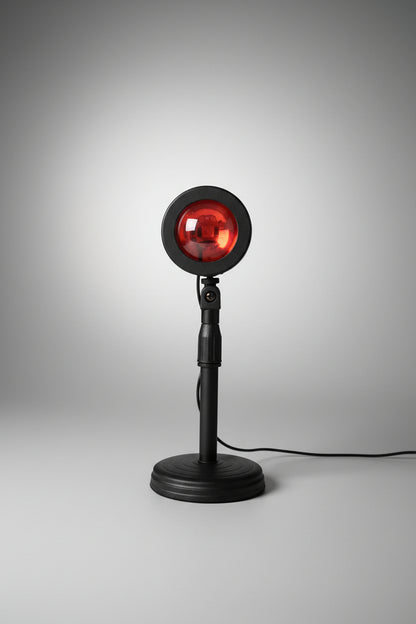 A floor lamp with a round orange light bulb projecting a sunset-like glow, mounted on a black base with a cord.