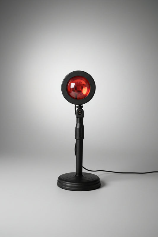 A floor lamp with a round orange light bulb projecting a sunset-like glow, mounted on a black base with a cord.