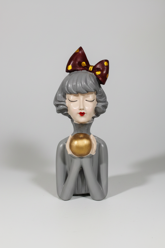 A modern resin figurine of a doll holding an apple, with a gray body and pink accents on the ears.