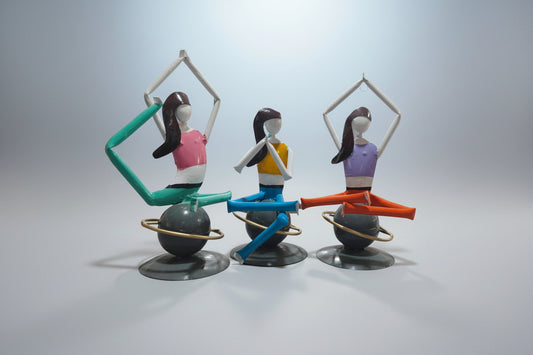 A metal decorative statue featuring three abstract representations of ladies in yoga poses. Each figure is primarily in one color with added details in contrasting colors.